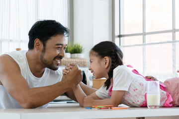 Bearded Asian young father and little mixed race daughter lying in kitchen doing arm wrestling...