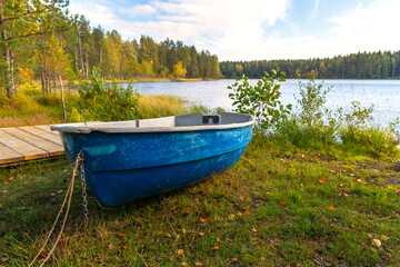 Autumn landscape, an old blue boat lies on the shore of a forest lake. The boat is pulled ashore for the winter for safety.