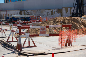 fenced area of the construction site. Red and white safety barriers enclose a pile of soil. There is warning sign on the barrier. Translation: "Danger area! Keep out!"