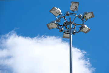 Projector stand made of several individual spotlights on the background of clear blue sky with clouds. Lighting  mast concept at the stadium, construction site or plant. Copy space for text