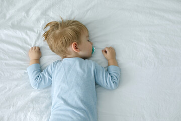 Sleeping adorable baby boy in bed with pacifier in the mouth