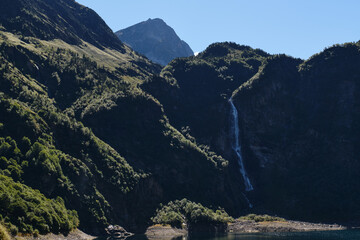 Lac d'Oô in the French Pyrenees is an artificial lake surrounded by large green mountains with a large waterfall.