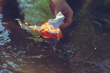 A mature man holds a burning piece of paper in his hand.