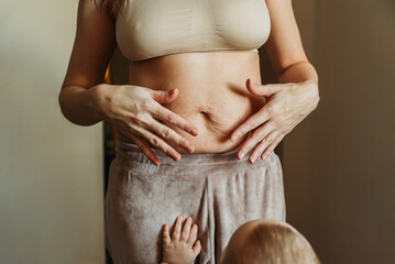 Little baby's hands on woman's belly full of stretch marks after pregnancy.