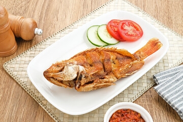 Fried Tilapia or Ikan Nila Goreng. Served on white plate with sambal (chilli sauce), cucumber and tomato slice. Selected focus.
