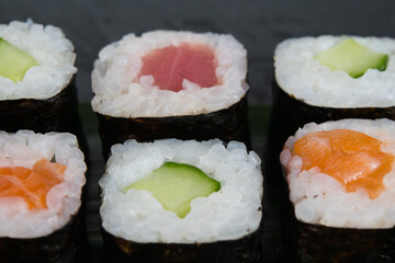 on a dark background, assorted Japanese delicacies, tuna, salmon and fresh cucumber rolls, close-up