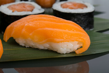 on a black background with reflection, on a bamboo leaf, Japanese rolls with salmon and sushi, close-up