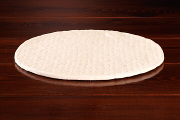 The dough is prepared as the basis for pizza. Frozen pizza base lies on a wooden table.