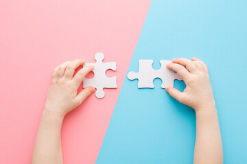 Baby hands playing and putting together white puzzle pieces on light blue pink table background. Pastel color. Closeup. Point of view shot. Children development. Two sides. Top down view.