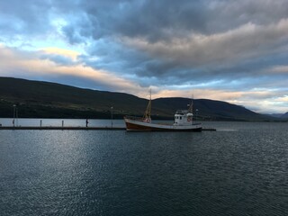 Obraz premium Boat moored at pier in Húsavík Harbor under cloud sky at sunset. Iceland.