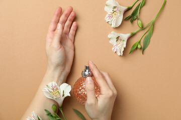 Female hands hold bottle of perfume on beige background with flowers
