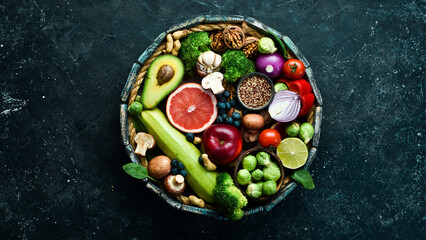 Set of healthy food in a wooden box: Green vegetables, avocado, broccoli, nuts, mushrooms, berries and spinach. On a black stone background. Top view. Copy space.