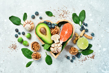 Foods good for the heart: nuts, salmon, avocados, spinach, mushrooms, berries. In a heart-shaped box. On a stone background. Top view. Copy space.
