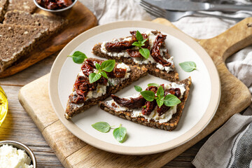 Bruschetta or wholegrain bread sandwich with cream cheese and sun-dried tomatoes. Crostini in a plate on a kitchen table