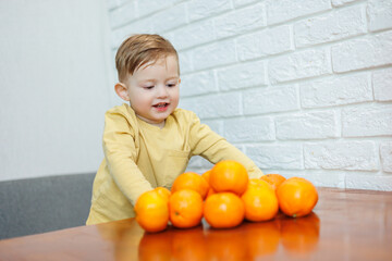 A little boy 2 years old holds tangerines in his hands. The kid wants to sit on citrus fruits for the first time.