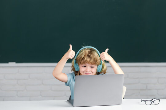 First day at school. Child boy with thumbs up in headphones using a laptop and study online with video call teacher at school. - Powered by Adobe