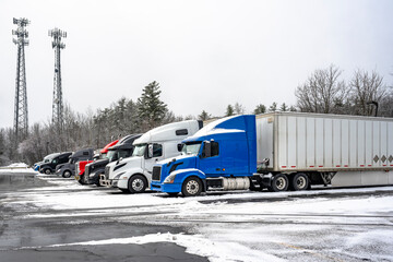 Big rigs semi trucks with different semi trailers standing for truck driver rest on the winter...