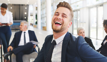 Smiling contributes to success. Cropped portrait of a handsome young businessman sitting and laughing while his colleagues work behind him in the office.