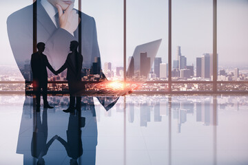 Abstract image of businessman using laptop in modern office interior with panoramic city view, businesspeople shaking hands and mock up place. Teamwork, leadership and technology concept.
