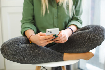 Woman using modern mobile phone at home during lockdown. Young female typing message in messenger app on modern smartphone device. Person communicating online with new dual camera cellphone