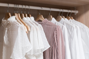 Clothes in the closet. Women's light vintage clothes on hangers in the closet of the dressing room. Fashion trends, textiles, recycling, second hand.