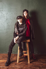 Two charming teenage girls with bright makeup, dressed in a grunge style, against a dark wall.
