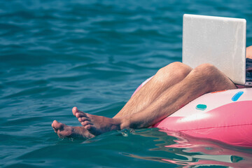 Working anywhere and any time concept.  Man freelancer working with laptop on inflatable ring in sea. Selective focus. Copy space for design.