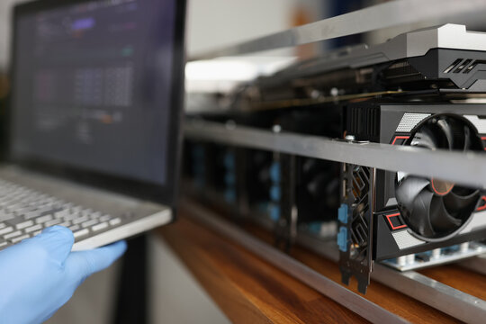 Master in rubber gloves holding laptop in front of mining farm closeup - Powered by Adobe