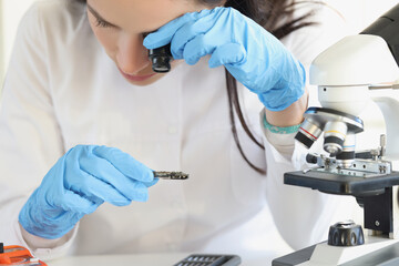 Woman scientist looking through magnifying glass at computer chip near microscope in laboratory