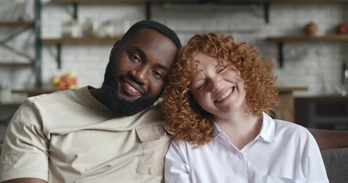 Portrait of adorable loving interracial couple, embracing each other, cute smiling with toothy smile looking at the camera posing on the kitchen background of their home apartment