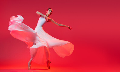 elegant ballerina in pointe shoes dancing in a long white skirt on a red background
