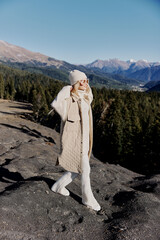 young woman in autumn clothes stands on a rock blue sky lifestyle