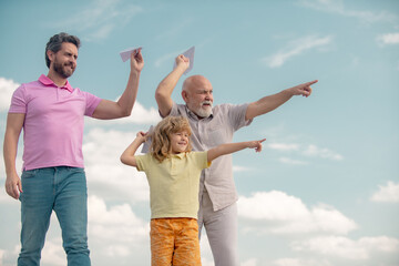 Three different generations ages grandfather father and child son playing with toy plane outdoors....
