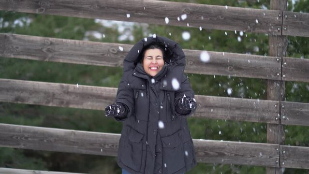 Chica joven guapa tirando nieve para el cielo con las manos y sonriendo a c&aacute;mara 