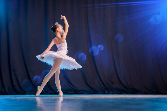 Fototapeta little girl ballerina is dancing on stage in white tutu on pointe shoes classic variation.