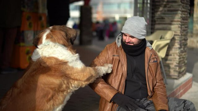 Chico alto  con gorro gris y barba sentado junto al perro mientras le acaricia