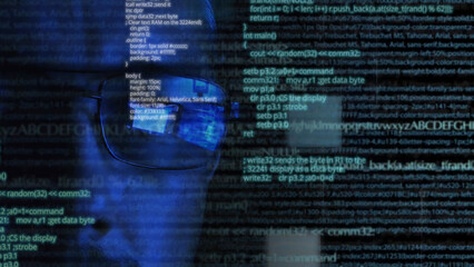 Programmer or hacker in glasses looking on monitor - software code reflecting in the glass and flying around. Caucasian man face in the dark. Digital technologies, software development. Blue colored.