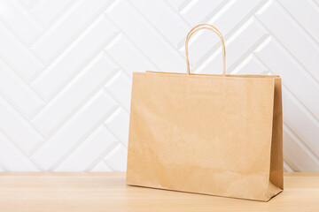 Paper shopping bag on the background of a white wall and a wooden table. Purchase and sale delivery...