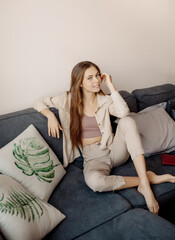 Obraz premium Young woman with book sitting at couch at home biophilic interior, many indoor trees