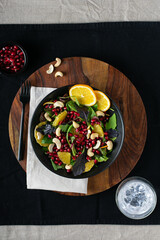 Fresh salad with orange and pomegranate seeds, baby spinach on wooden background. Top view. Copy space