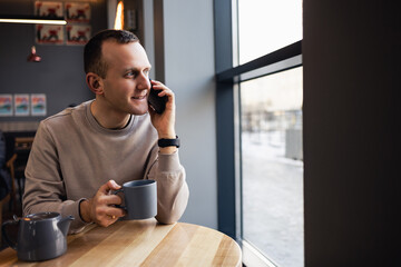 A young man is talking on his cell phone in a bar and drinking coffee. Young fashionable man drinking espresso coffee in a city cafe during lunch and working