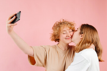 Happy lesbian couple taking selfies together. Two lesbian pretty women having fun celebrating their feelings on Valentines Day. Redhead girl is being kissed at the cheek, feeling amazing