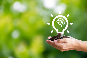 In hand holding a light bulb on green background with brain icon in the light bulb. Demonstrate an...