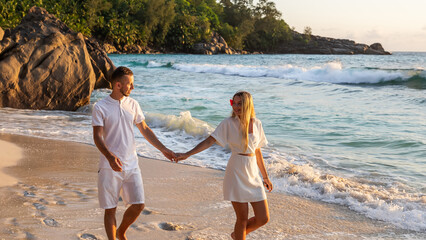 Honeymoon romantic couple in love holding hands walking on beautiful sunset at beach in waterfront. Lovers or newlywed married young couple by the sea enjoying relaxed vacation travel holiday. Hawaii.
