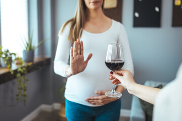 Close up of pregnant woman at home refuses to drink wine and makes stop gesture to the glass. No alcohol during pregnancy concept