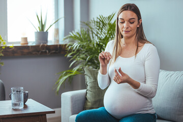 Pregnant woman sitting at a living room of a house with people, introducing a nasal swab in the...