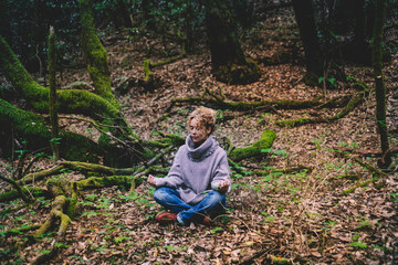 Naklejka na ściany i meble One woman sitting in loto yoga position on the ground foliage in the nature outdoors park. Concept of healthy lifestyle and mindfulness exercise meditation. Human nature connection