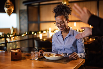 Fototapeta na wymiar Happy African-American woman, preparing to take a bite of her food, talking to the waiter.