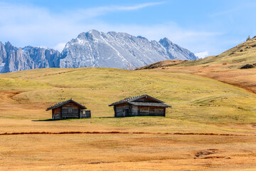 Two alpine huts on Seiser Alm plateau in autumn on the background of Langkofel Group mountains