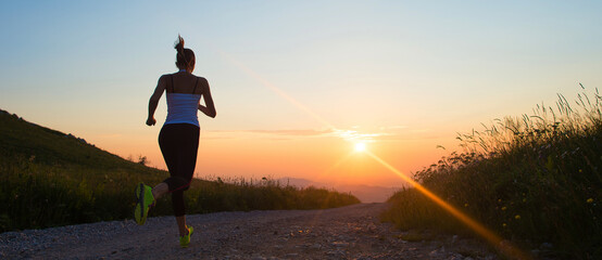 woman running on a mountain trail at summer sunset banner size